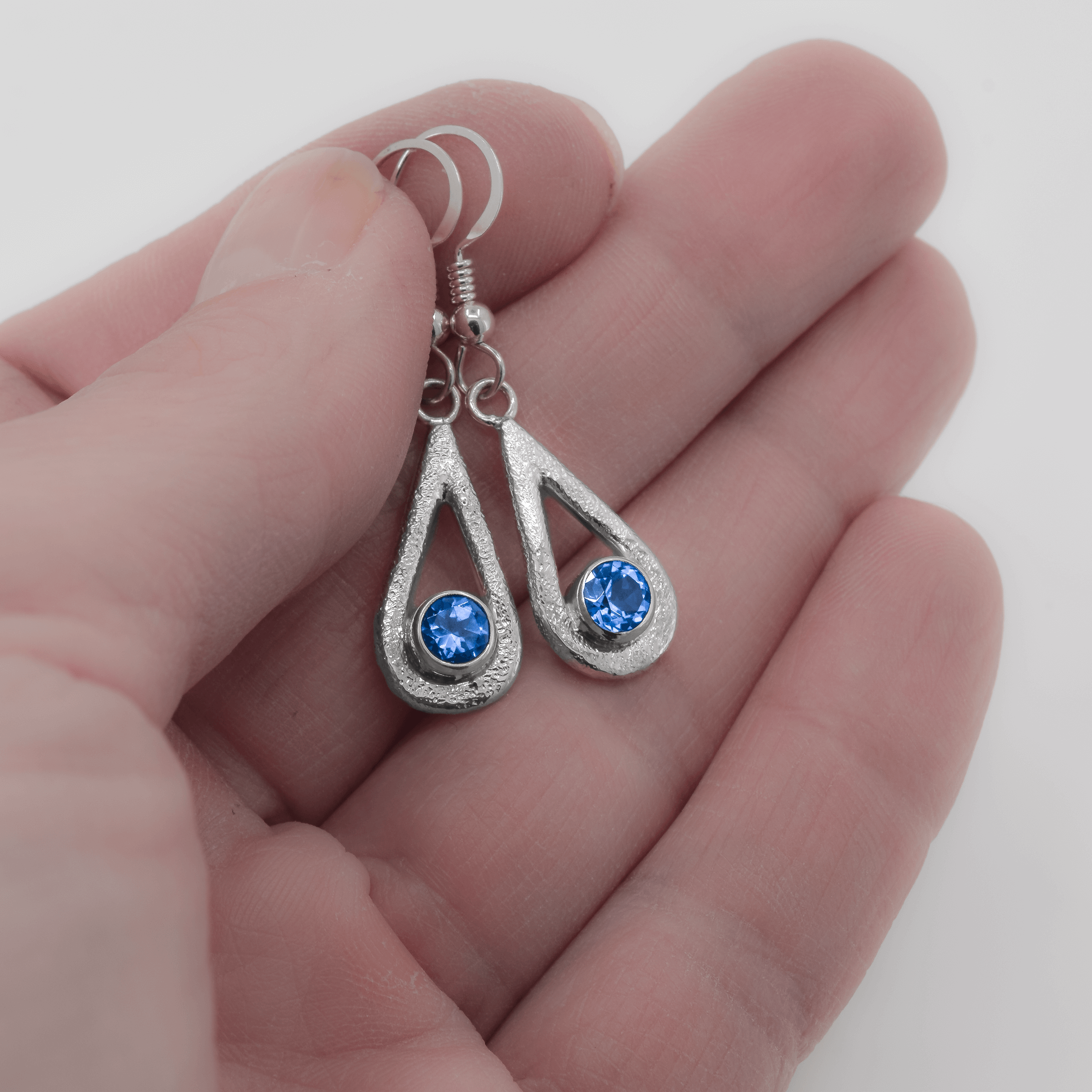 Ice Blue topaz teardrop shaped dangle earrings in sterling silver, featuring a stardust texture , shown in hand for scale.