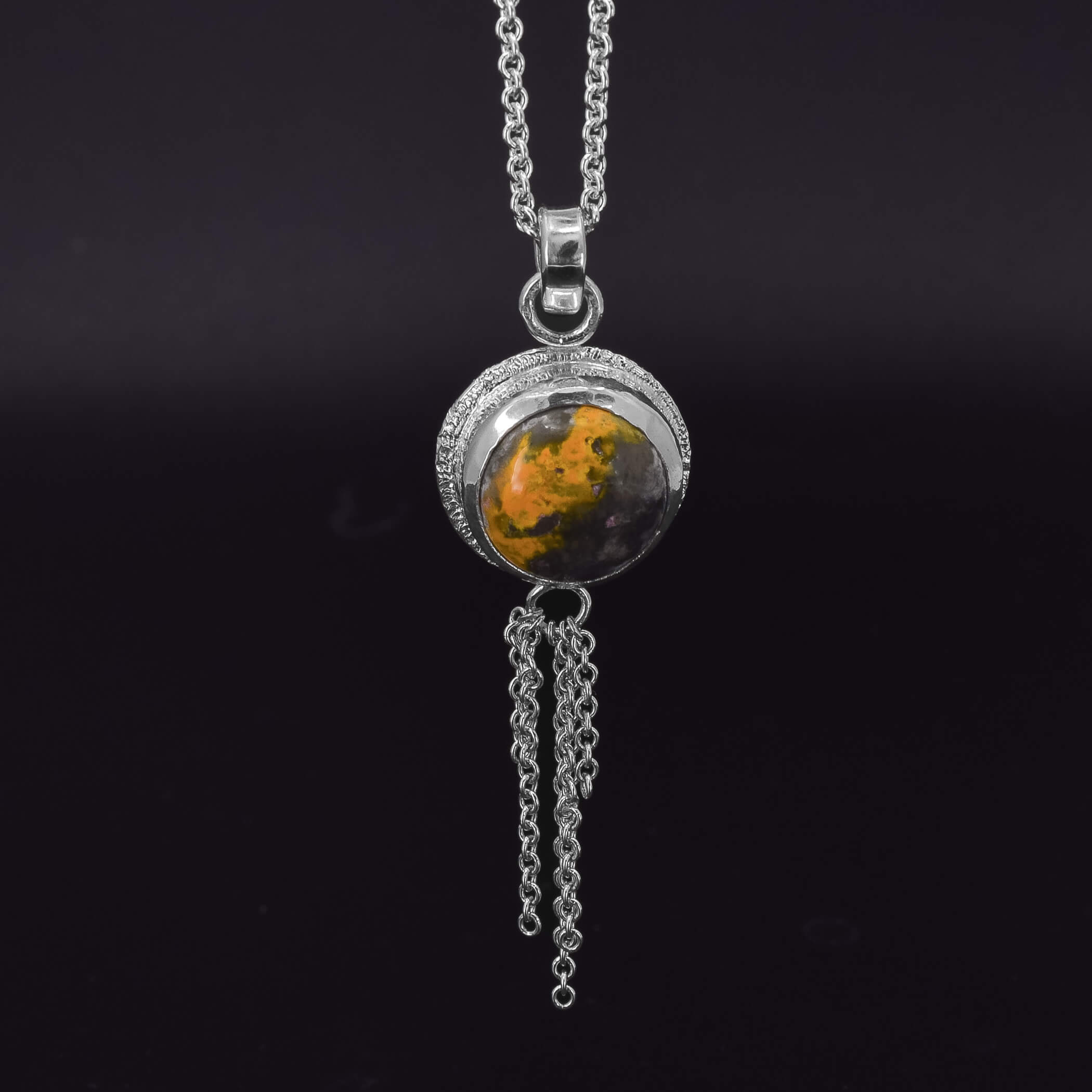 sterling silver necklace featuring a round bumblebee jasper stone, with a stardust texture around the edges and a chain embellishment at the bottom of the pendant on a black background