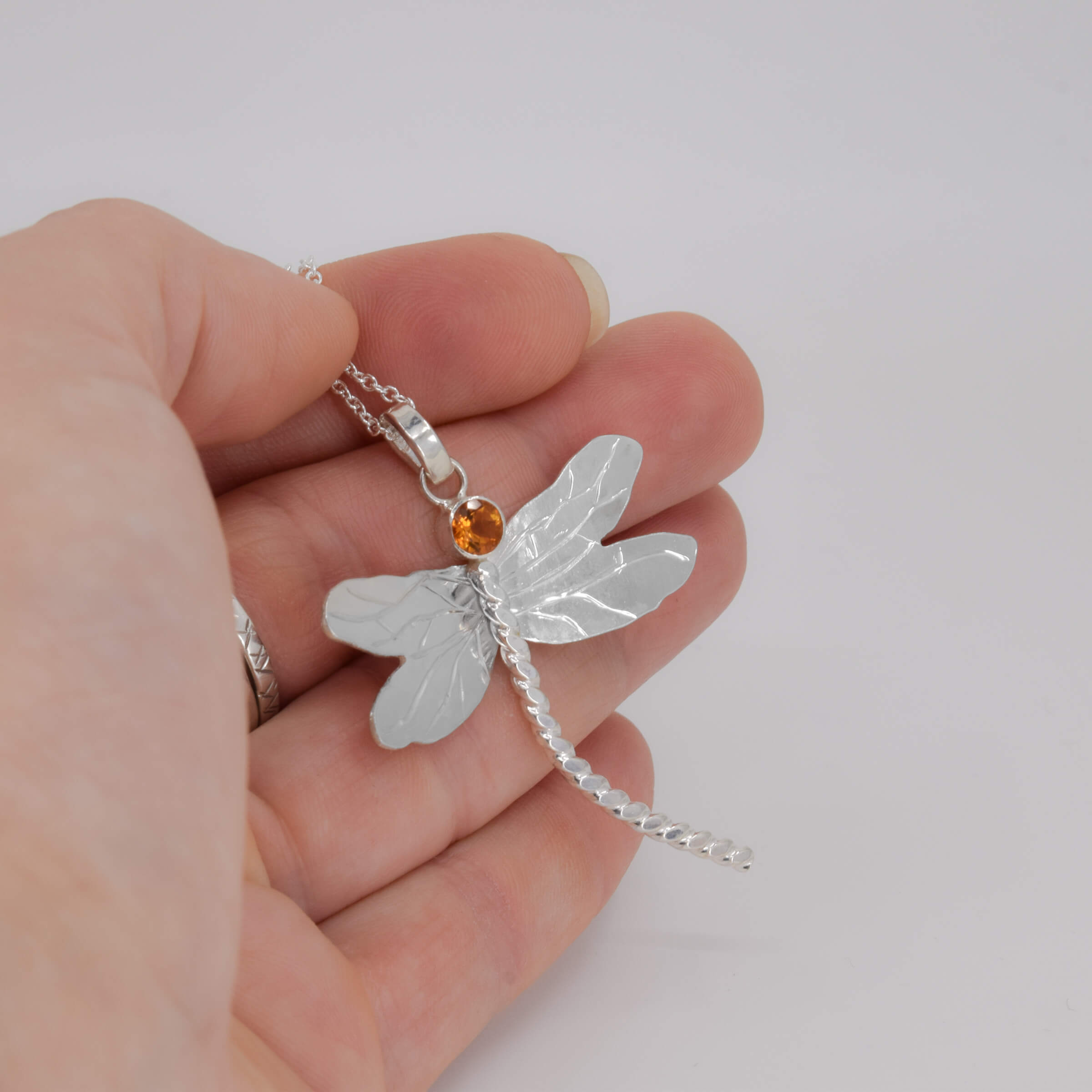 Silver dragonfly pendant with a small citrine gemstone held in a hand against a white background