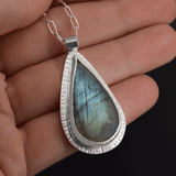 green statement pendant featuring a green labradorite stone, hanging on a paperclip style chain shown in hand for scale