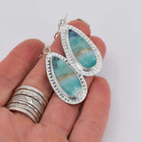 Teardrop shaped petrified wood opal dangle earrings in sterling silver  with a hand textured border around the stones shown in hand for size.