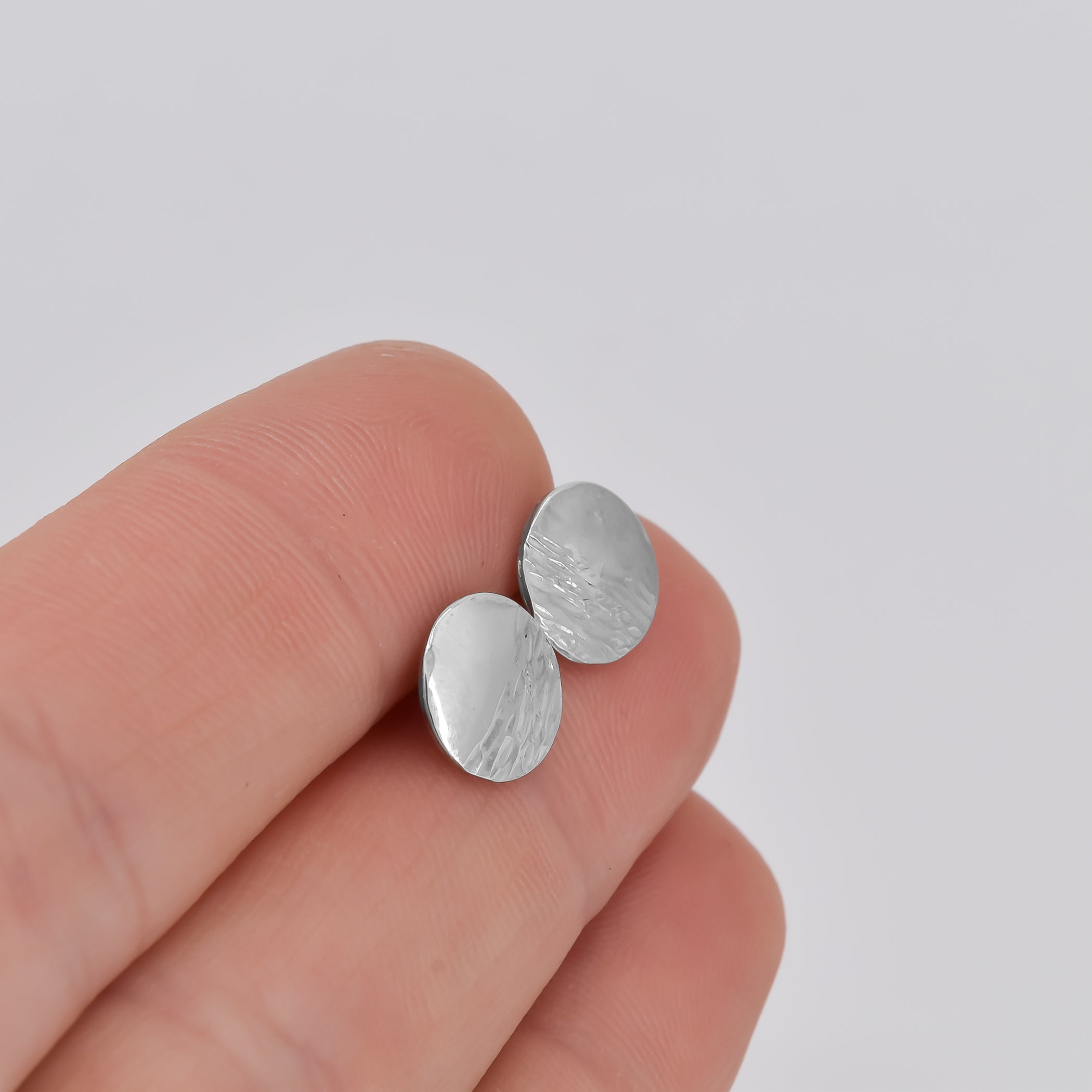 Textured circle stud earrings sterling silver shown in hand for scale